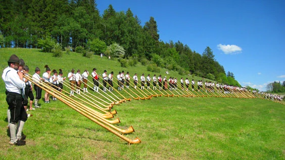 Männer in Trachten spielen das Alphorn im Allgäu